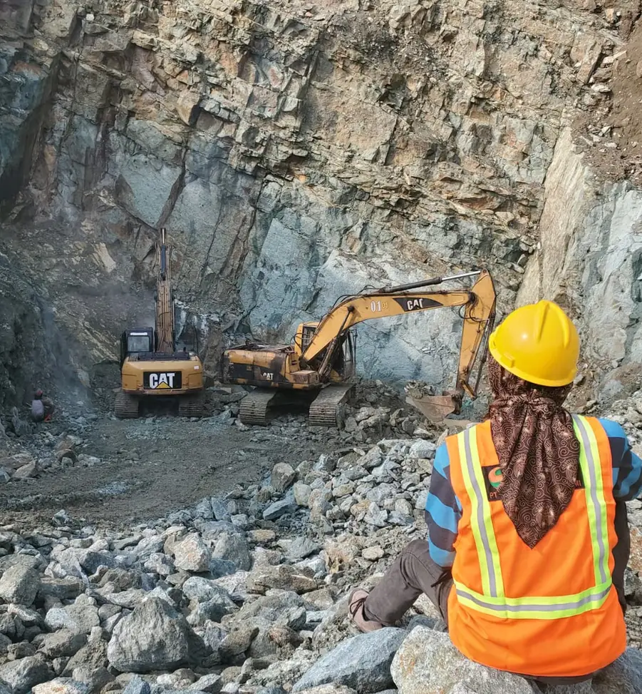 Excavator and worker at a stone quarry face